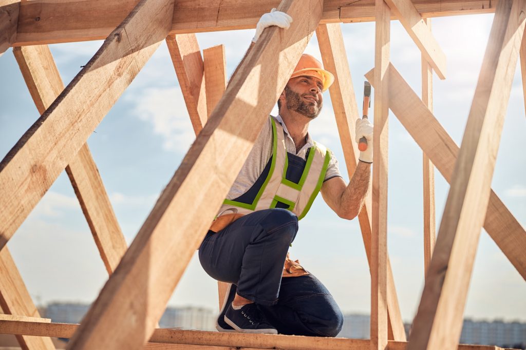 joyous-construction-site-worker-with-hammer-building-a-roof-carcass