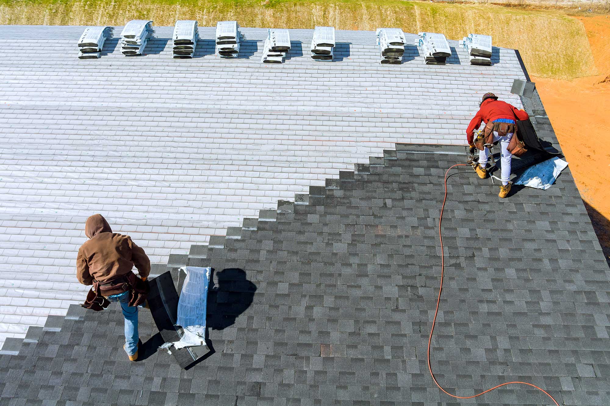Workers install asphalt shingles on a residential roof.